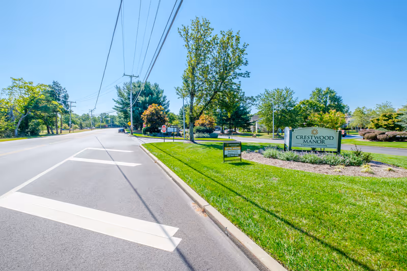 Roadside view of the Crestwood Manor entrance sign and landscaped grounds along a sunny suburban street.