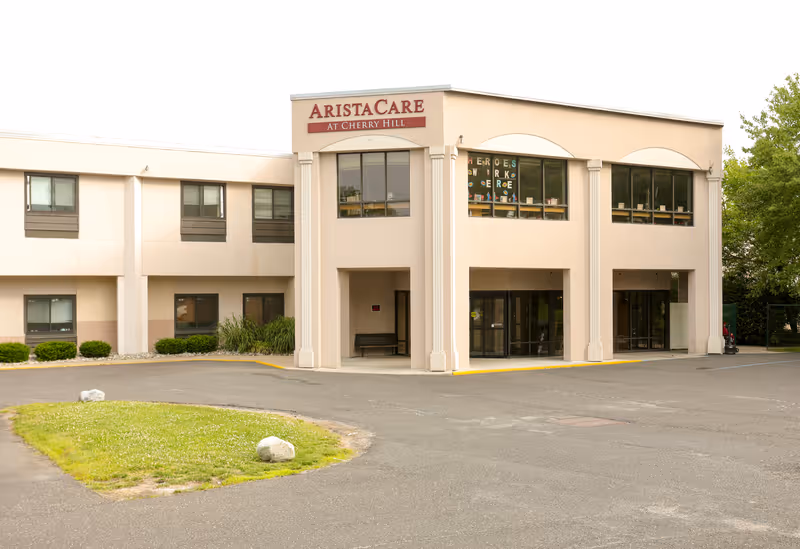 Front exterior of the AristaCare at Cherry Hill two-story building with main entrance and parking area.