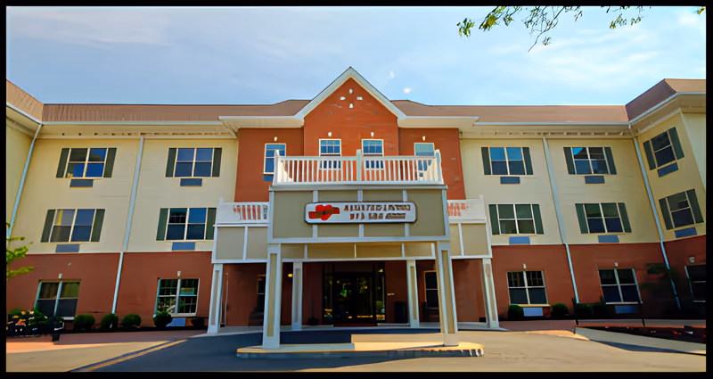 Front exterior view of a three-story assisted living facility building with a covered entrance and multiple windows, under a clear blue sky.