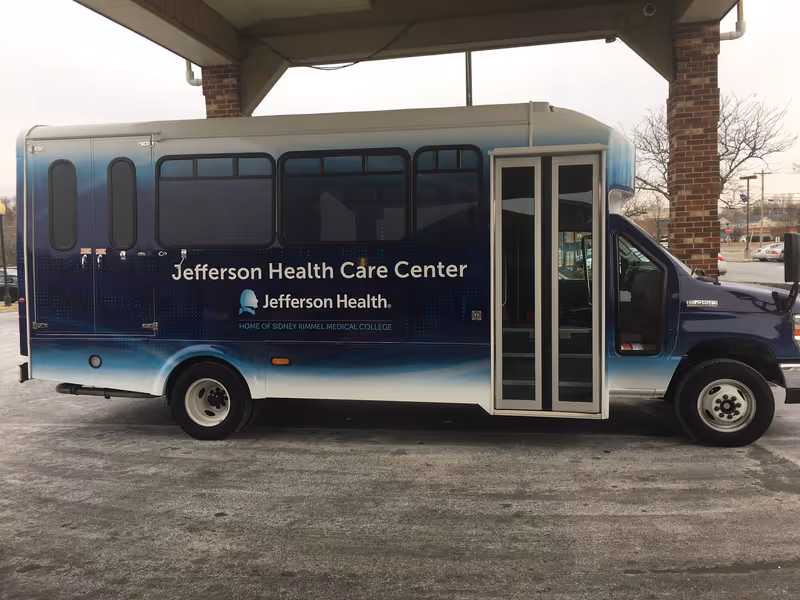 A Jefferson Health Care Center shuttle bus parked under a canopy with its passenger doors visible.
