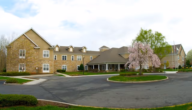 Front exterior of a two-story assisted living building with a circular driveway and a blooming pink tree.