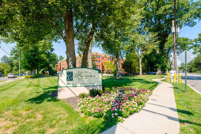 Landscaped front lawn and flowerbed with a Five Star Premier Residences of Teaneck sign in front of a brick residence and sidewalk.