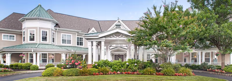 Front exterior of Sunrise of Wall senior living facility with a two-story building, covered porte-cochere, and landscaped gardens and trees.
