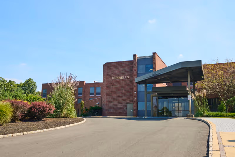 Brick-front Runnells rehabilitation building with a covered drop-off canopy, glass entrance, and landscaped driveway.