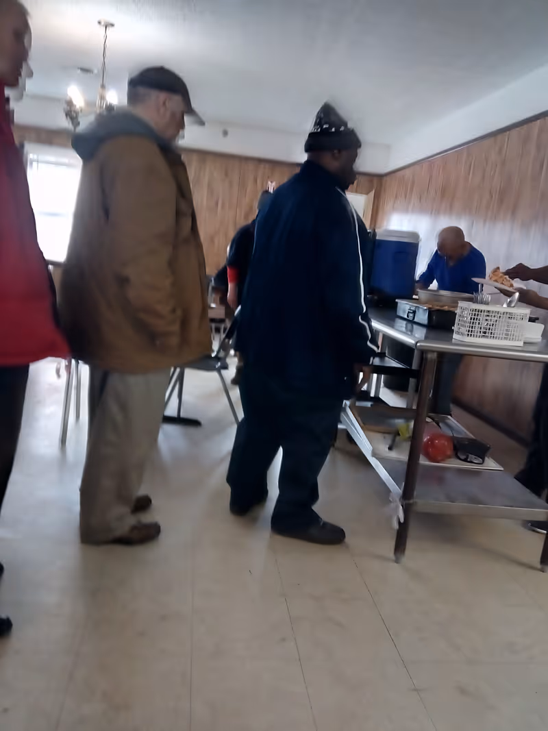 Several people standing in line at a serving table inside a wood-paneled dining room.