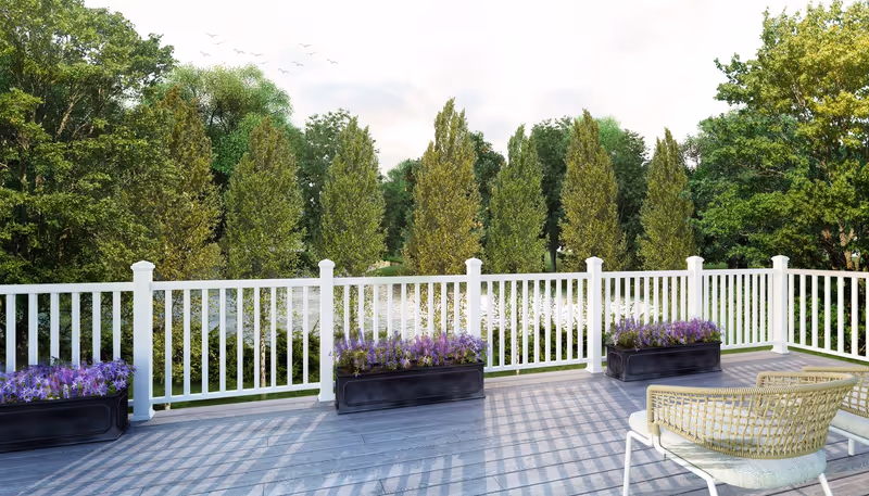 Wooden deck with white railing, planters of purple flowers, and chairs overlooking a pond and trees.