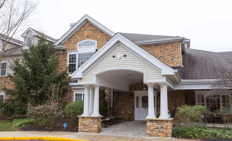 Front entrance of a stone-and-brick senior living building with a covered porte-cochere supported by white columns.