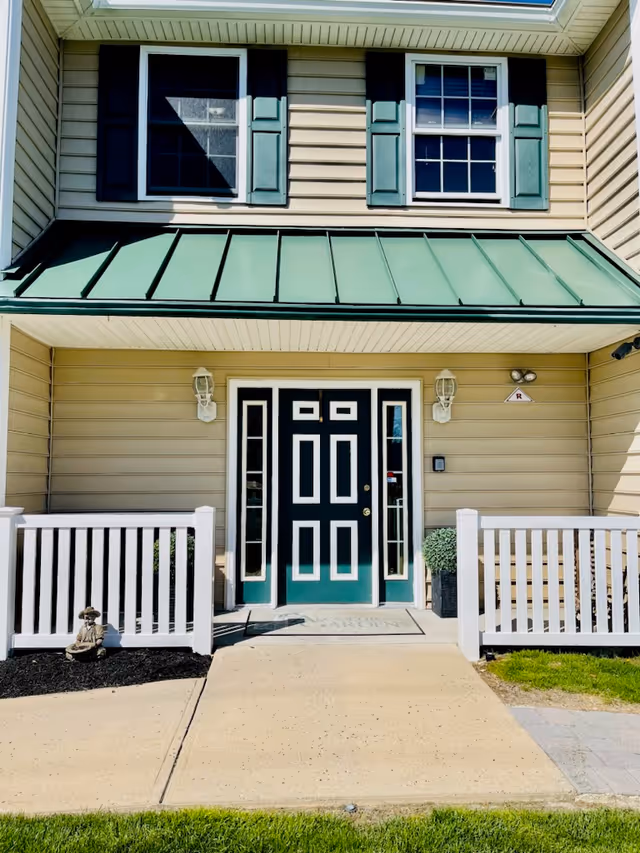 Entrance of a beige building with a green-trimmed double door, white porch railings, and upper windows.