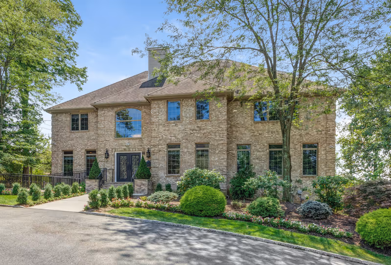 Two-story brick building with large windows, a double-door entrance, and landscaped grounds with trees and shrubs.