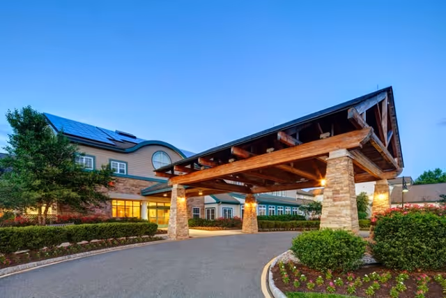 Covered porte-cochère with wooden beams and stone pillars at the entrance of the Stonebridge at Montgomery building at dusk.