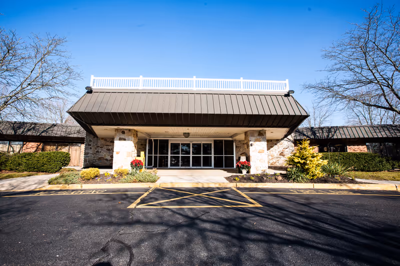Front exterior view of Hammonton Center building with stone pillars, large glass entrance doors, landscaped bushes and flowers, and a clear blue sky.