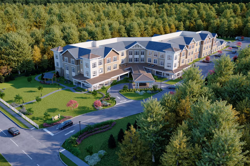 Aerial view of a three-story Sunrise of Livingston senior living building surrounded by trees, landscaped lawns, driveways, and parking areas.