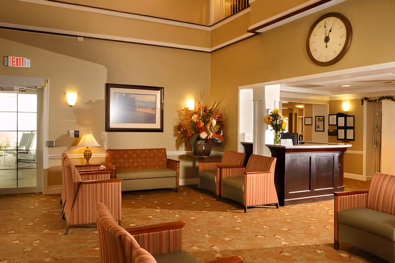 Lobby seating area with upholstered chairs and sofas, a reception desk, wall clock, and a floral arrangement.