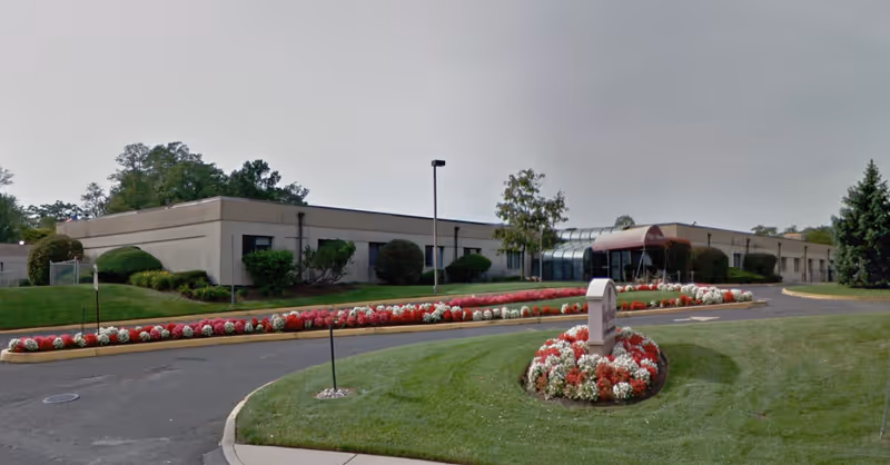 Single-story care center building with a glass-covered entrance, circular driveway, and landscaped flowerbeds in front.