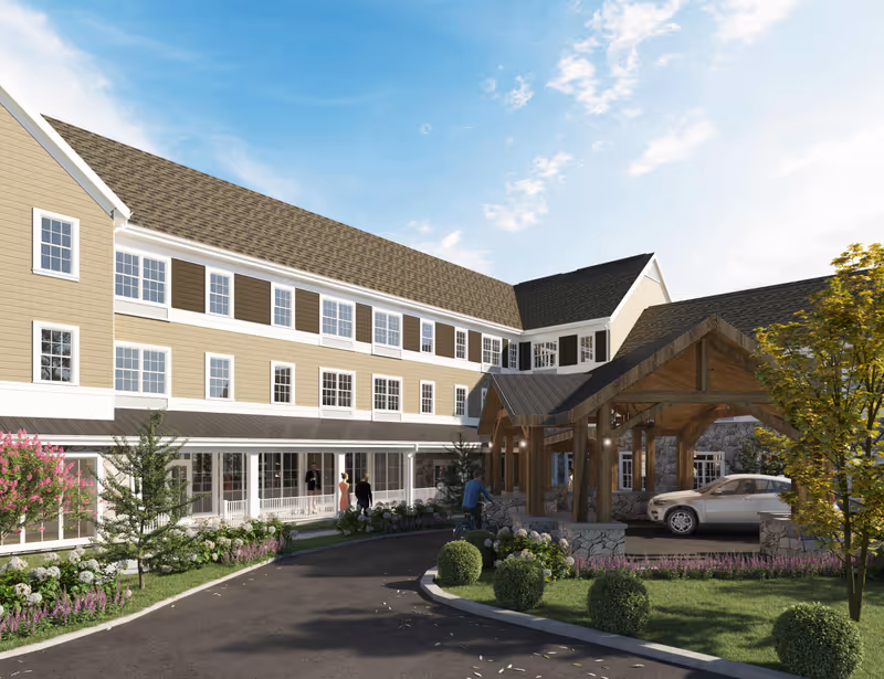 Exterior view of Ridgewood Senior Living at Historic Smithville showing a large multi-story building with beige siding, white trim, and multiple windows. There is a covered entrance with wooden beams and stone pillars, a driveway with a parked car, landscaped greenery, and a few people walking near the entrance under a partly cloudy sky.