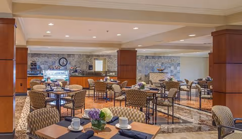 Spacious dining area with multiple tables and chairs, a service counter with a display case, and floral centerpieces on tables.