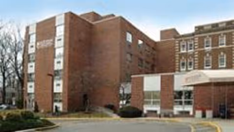 Exterior view of a multi-story brick building with several windows, part of a senior living facility named Care Connection Rahway, with a driveway and some landscaping in front.