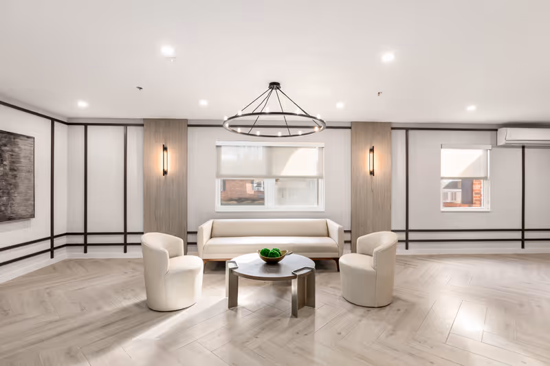 Bright modern lounge with a sofa and three upholstered chairs arranged around a round coffee table beneath a circular chandelier.