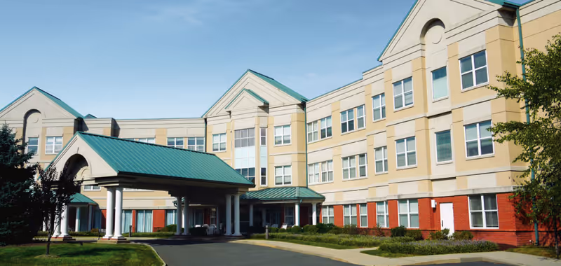 Front exterior of a multi-story senior living/post-acute care building with a covered entrance and green roofs.