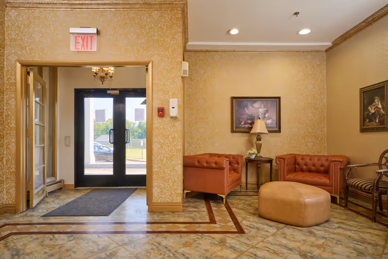 Lobby seating area with leather sofas, a round ottoman, side table and lamp beside double glass exit doors under an EXIT sign.