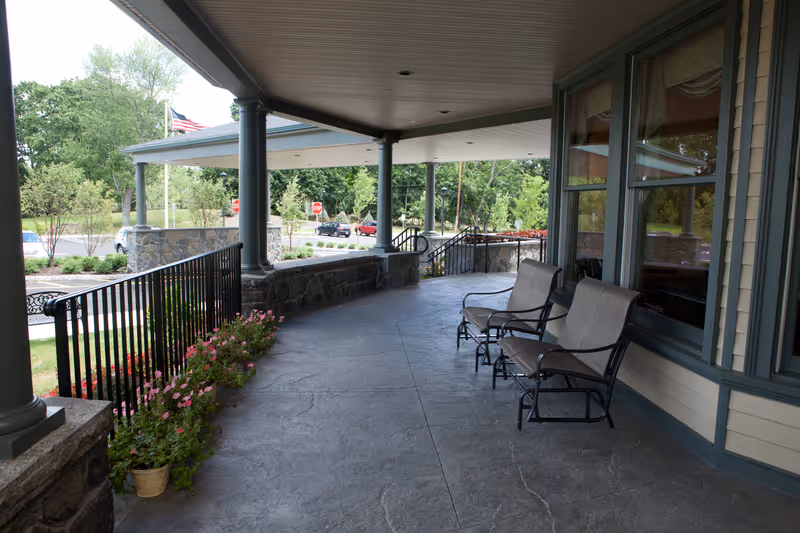 Covered front porch with chairs, columns, and flower planters overlooking the driveway and street.