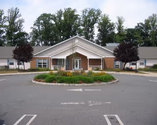 Front entrance of a single-story care facility with a covered portico, circular driveway and landscaped center island.