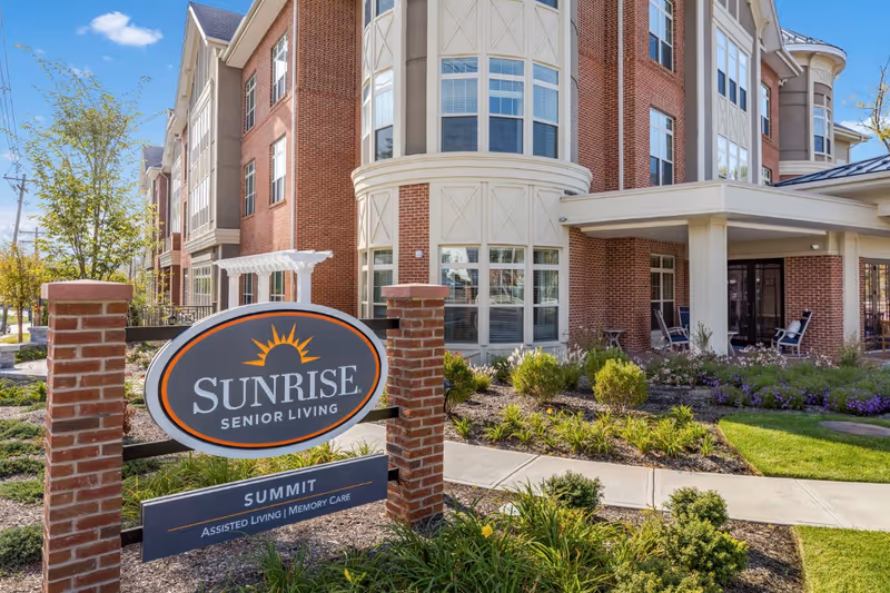 Exterior front of the Sunrise of Summit senior living building with landscaped entrance and a prominent Sunrise Senior Living sign.