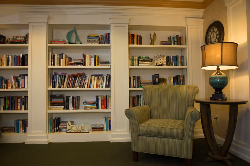 Cozy reading nook with built-in white bookshelves filled with books, a striped armchair, and a side table with a lamp.