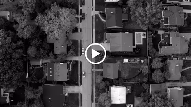 Aerial black and white view of a suburban neighborhood showing houses, trees, and streets from above.