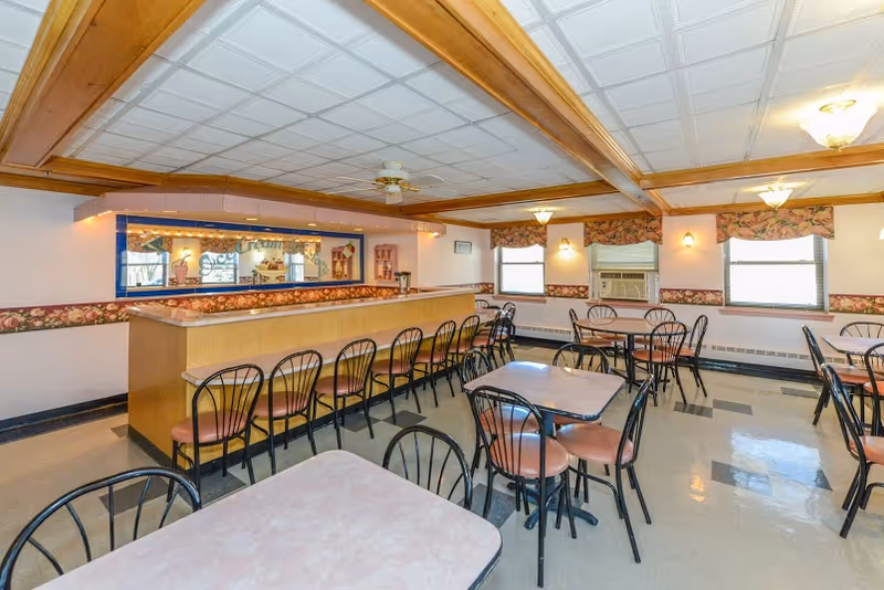 Dining room with multiple tables and chairs and a long wooden counter/bar under coffered ceiling beams.