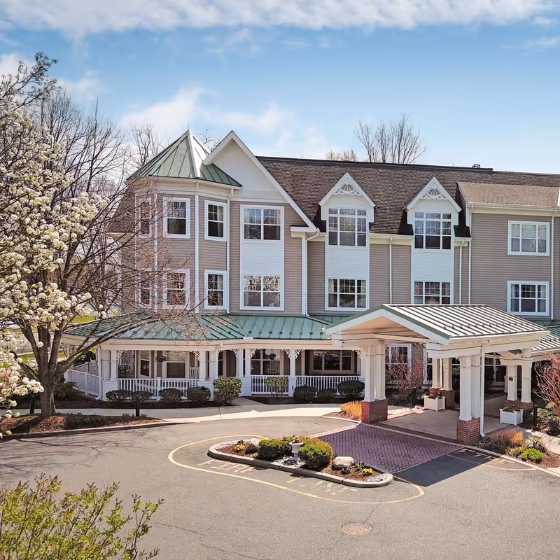 Three-story residential building with a green metal roof, covered porte-cochère, wraparound porch, and landscaped driveway.