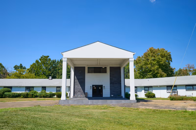 Front view of a white single-story building with a columned covered entrance and a grassy lawn.