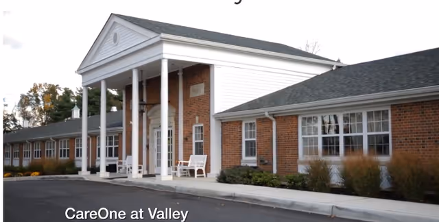 Front entrance of a single-story brick senior living building with white columns and benches.