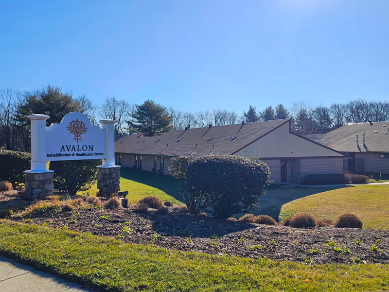 Exterior view of Avalon Rehabilitation & Healthcare Center sign and low single-story building with landscaped grounds under a clear blue sky.