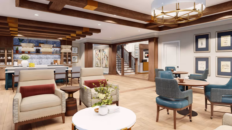 Open, warmly furnished communal living area with armchairs, small dining tables, and a kitchen/bar in the background.