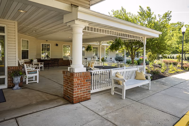 Covered outdoor porch at Mattison Crossing with white benches, columns, and potted plants.