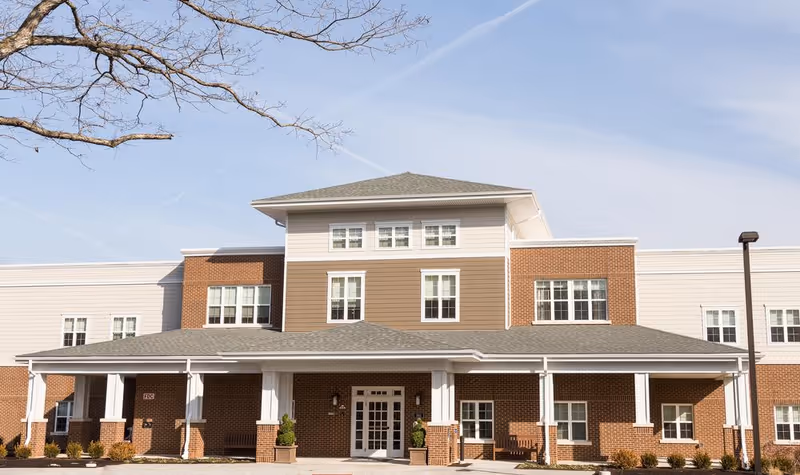 Front exterior of a three-story brick and siding senior living building with a covered entrance and multiple windows.