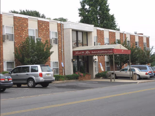 Exterior view of Laurel Bay Health & Rehabilitation Center, a two-story brick and concrete building with a maroon awning over the entrance. Several cars are parked in front along the street.