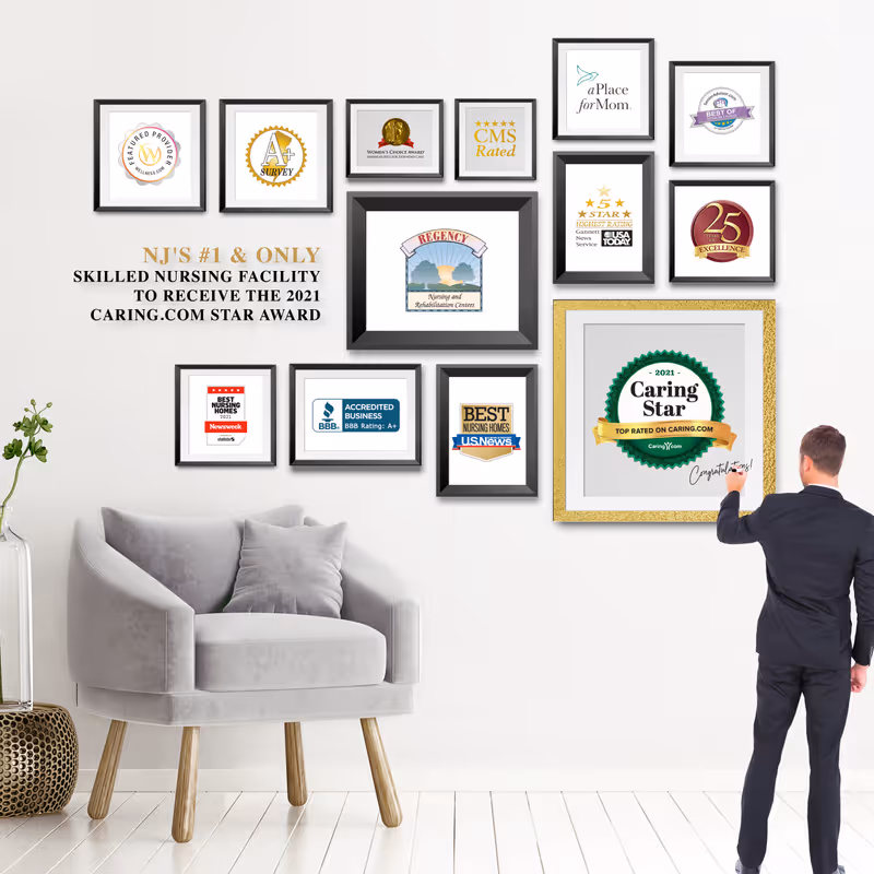 A modern interior wall displaying multiple framed awards and recognitions for Regency Nursing and Rehabilitation Centers. A man in a suit is signing or pointing at a large framed Caring Star 2021 award. A gray armchair with a cushion and a small plant in a vase are positioned to the left.