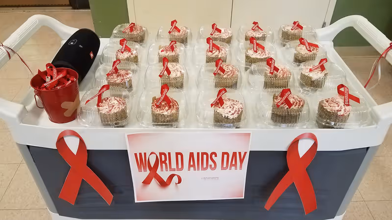 A service cart holding individually packaged cupcakes topped with red AIDS awareness ribbons and a sign reading "World AIDS Day".