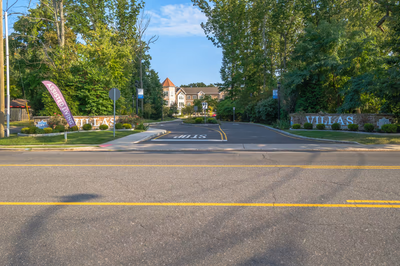 Tree-lined entrance driveway and signage reading 'VILLAS' with the senior living building visible in the background.