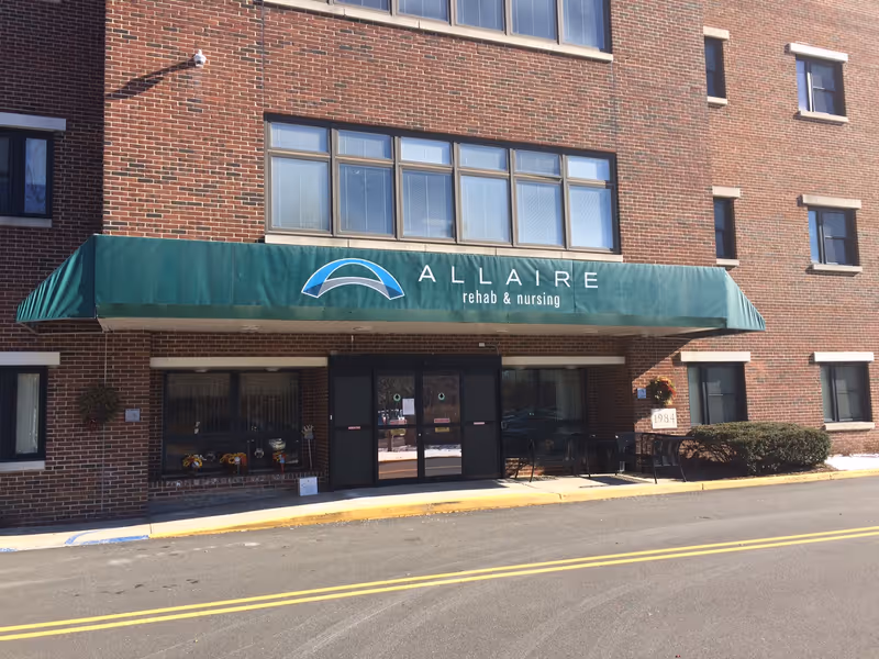 Brick exterior of Allaire Rehab & Nursing with a green awning over the main entrance.