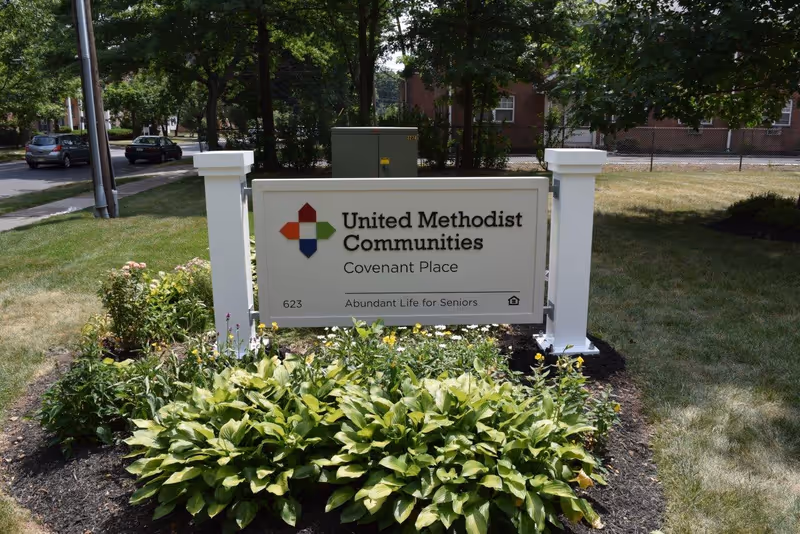 A landscaped outdoor sign reading "United Methodist Communities Covenant Place" on a lawn with shrubs and trees behind it.