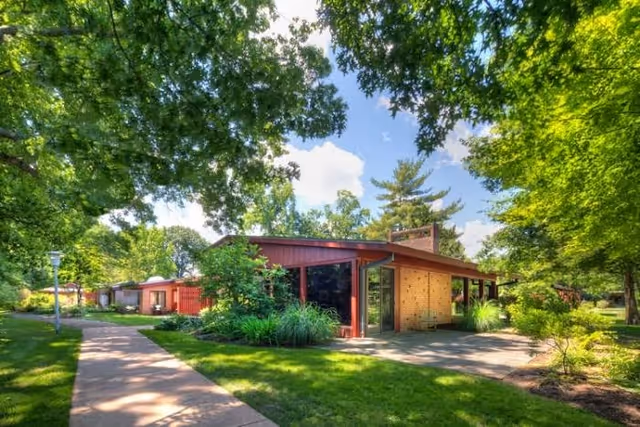 Single-story midcentury-style building surrounded by trees, lawn, and a sidewalk on a sunny day.