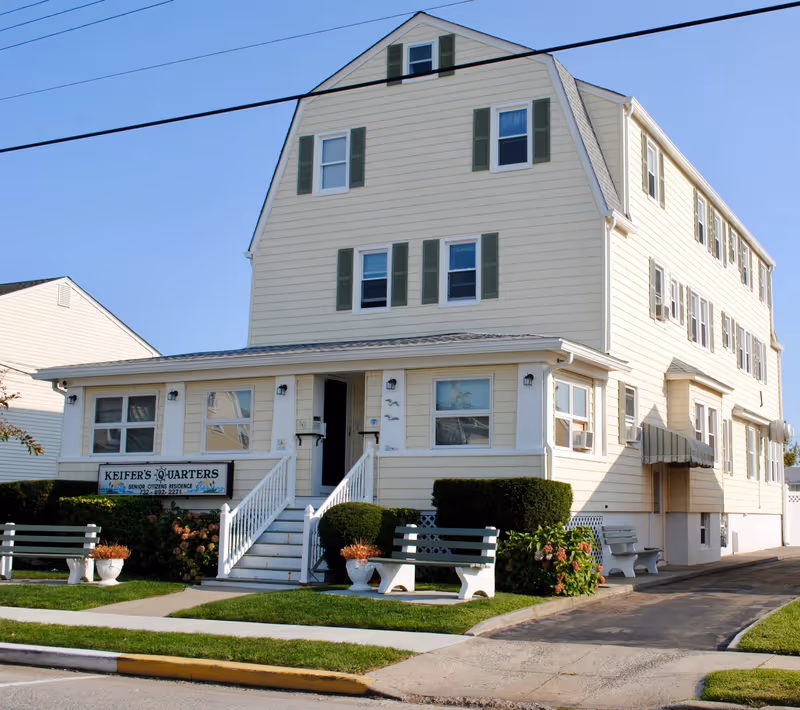 Three-story light yellow building labeled "Keifer's Quarters" with front steps, benches, and landscaping.