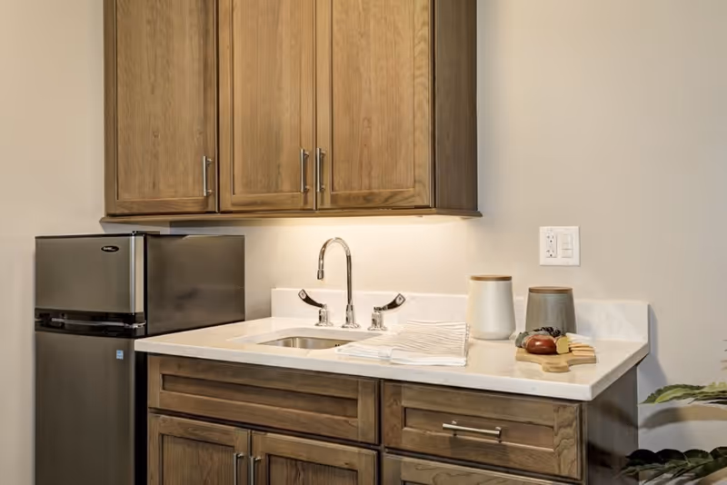 Small kitchenette with wooden cabinets, a countertop sink, mini refrigerator, and decorative canisters.